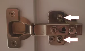 Illustration des vis de fixation du support de charnière à desserrer pour monter ou descendre une porte de placard affaissée.