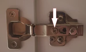 Gros plan sur la vis centrale d'une charnière permettant d'ajuster l'écart latéral entre deux portes de placard.