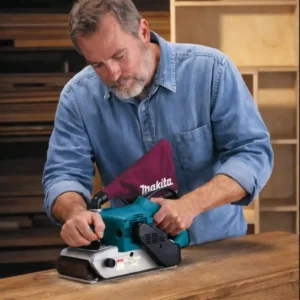 Ponceuse à Bande Ponceuse à bande Makita utilisée pour le ponçage d’un plateau en chêne lors d’une rénovation de meuble.