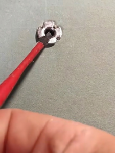 Gros plan d'un tournevis plat inséré dans la collerette d'une cheville Molly pour la casser et l'extraire d'un mur en placo propre.
