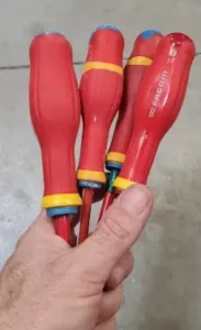 Main d'un électricien utilisant un tournevis isolé professionnel pour le serrage des disjoncteurs dans un tableau électrique